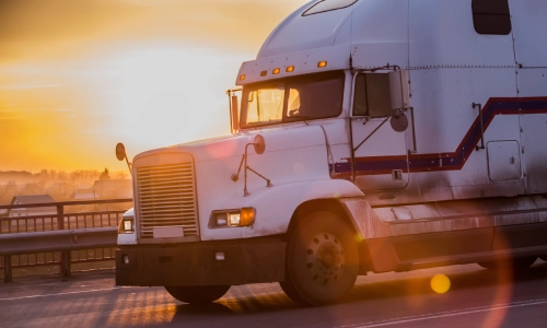 ਪਿਛੋਕੜ ਵਿੱਚ ਸੂਰਜ ਡੁੱਬਣ ਦੇ ਨਾਲ ਮਾਲ ਵਾਹਕ ਟਰੱਕ