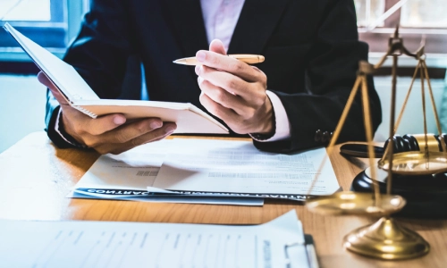 A California personal injury lawyer holding an open notebook in their right hand and a pen in the left sits at a desk with documents placed on top.