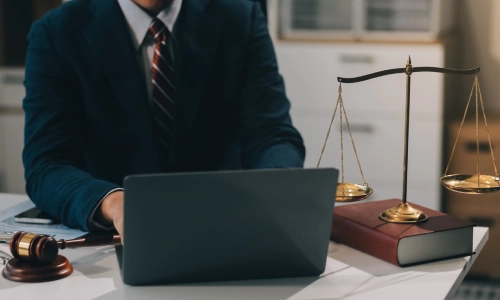 A rideshare accident lawyer serving California is working on a laptop placed in between a hammer and gavel and balance scales on top of an office desk