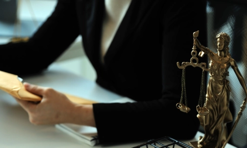 A California personal injury lawyer is holding a closed envelope with both hands while sitting at an office desk with a statue of lady justice