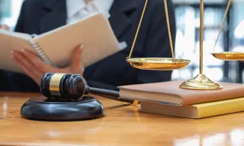 A California personal injury lawyer is sitting in the background and reading an open notebook in their left hand while balance scales sit in the foreground