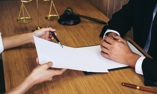 A California dog bite lawyer asks a client to sign a contract as they point to the document using a pen