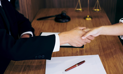 A California worker's compensation lawyer shaking hands with a satisfied client sitting across the table