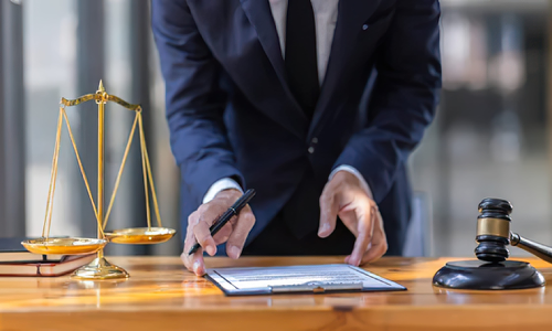 A California personal injury lawyer stands leaning over an office desk as he picks up a document lying on the table