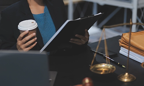 A car accident lawyer with a cup of coffee in hand and reviewing a car accident report on her clipboard.