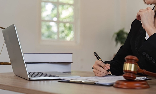 A pedestrian accident lawyer taking notes while comparing to a document on an open laptop