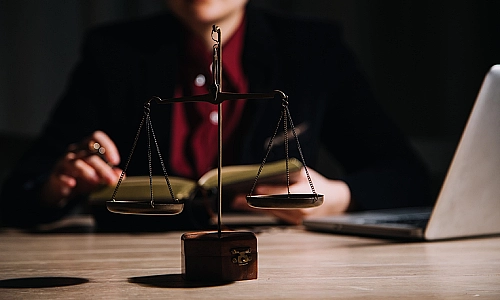 A personal injury lawyer reading a law book and sitting at an office desk with an open laptop